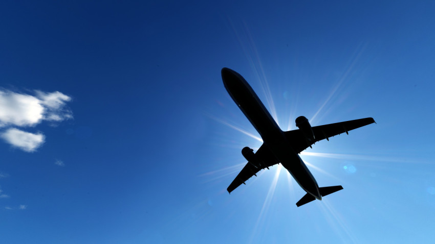 Photorealistic 3d render of a flying airplane against the background of the sun and blue sky